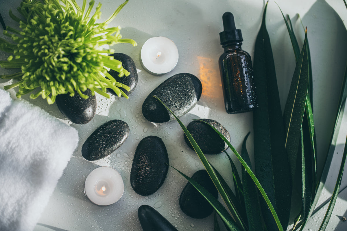 Natural spa stones, candles, greenery and a botanical serum bottle